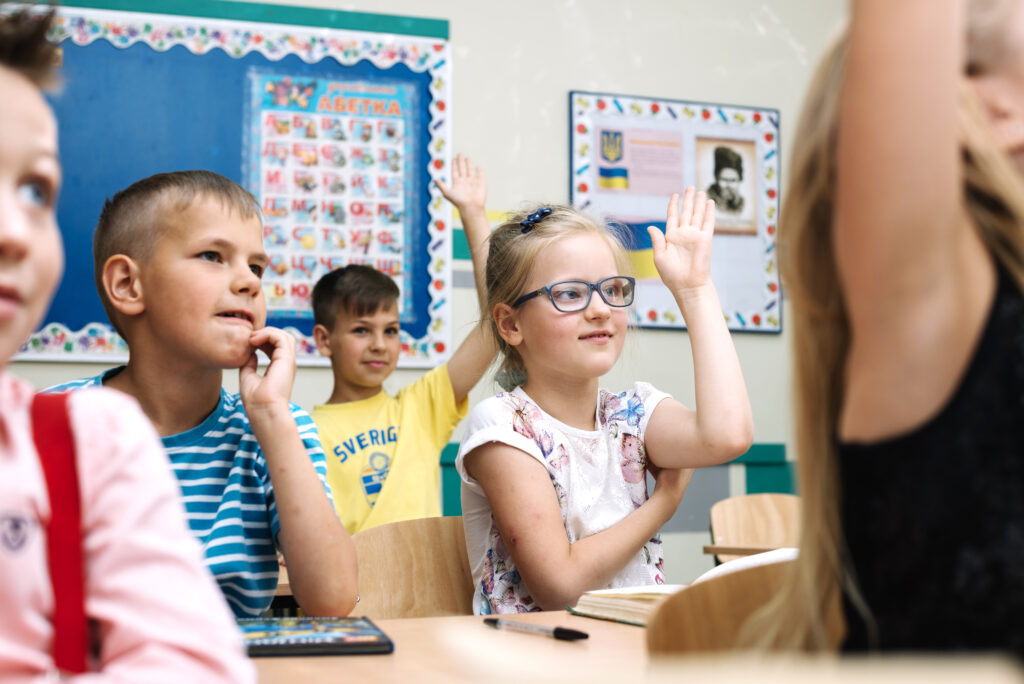 kids-sitting-school-desks-raising-hands