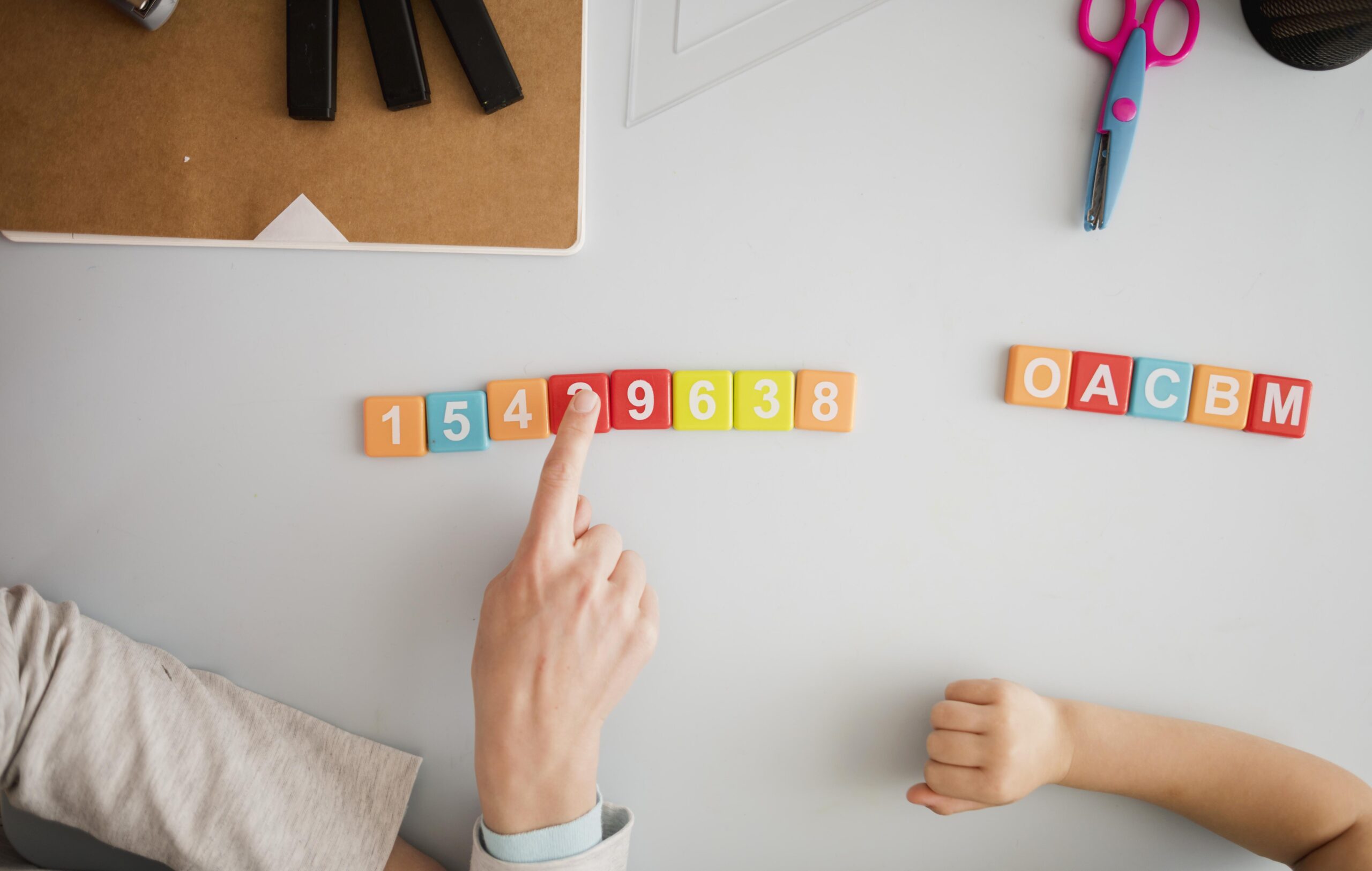 top-view-tutor-teaching-child-desk-about-numbers-letters